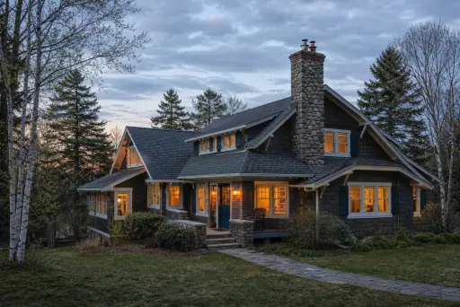 A 1950s Craftsman house with a stone masonry chimney and warm lamp-lit windows; illustrative image