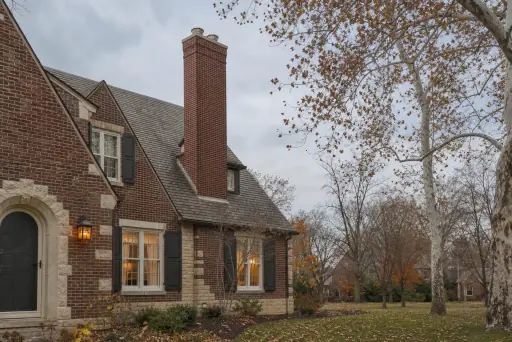 A 1940s Tudor revival house in soft daylight with a red brick chimney with a concrete crown standing clear above the roofline; illustrative image
