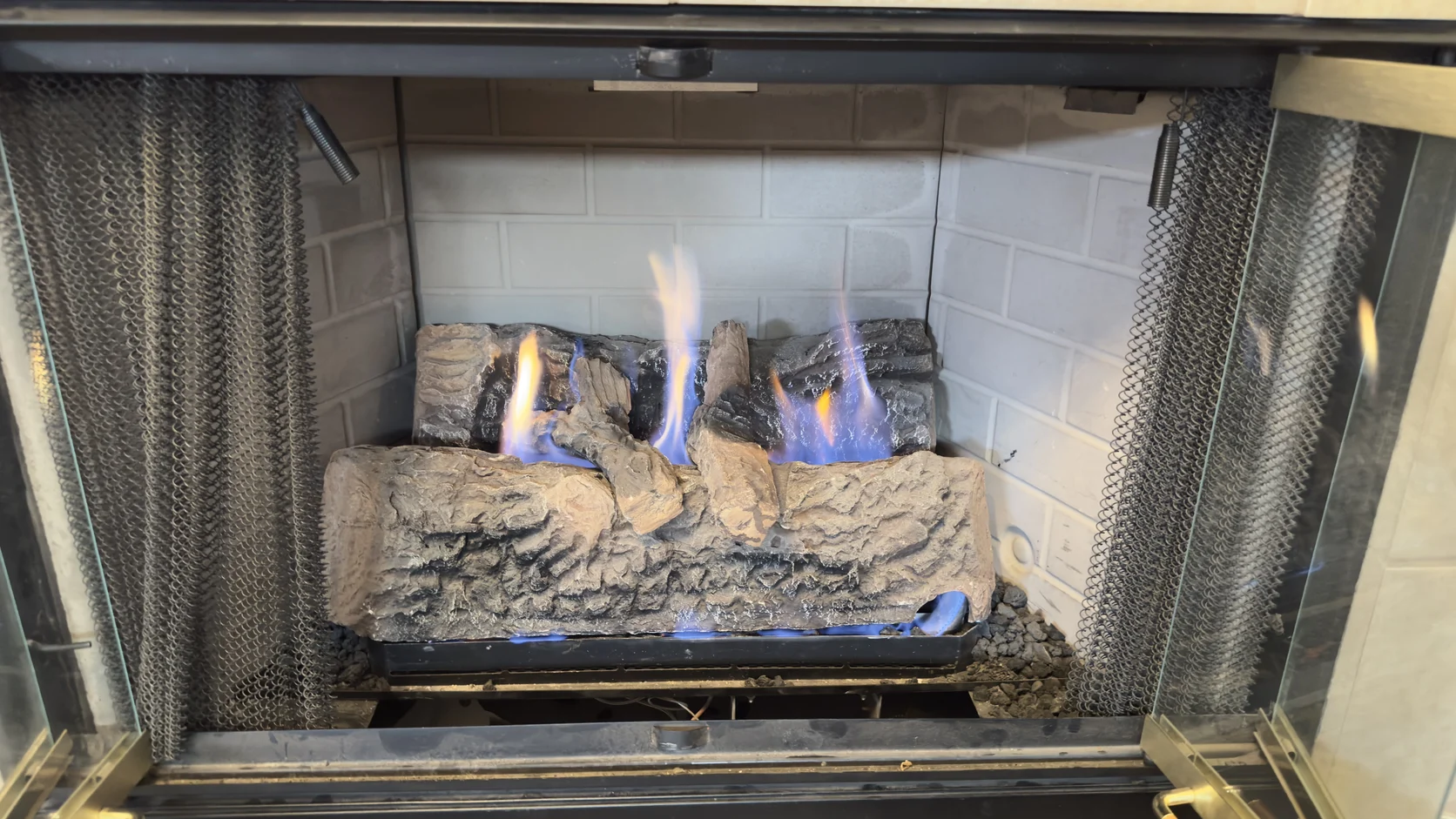 Gas log set with blue flames behind a mesh screen