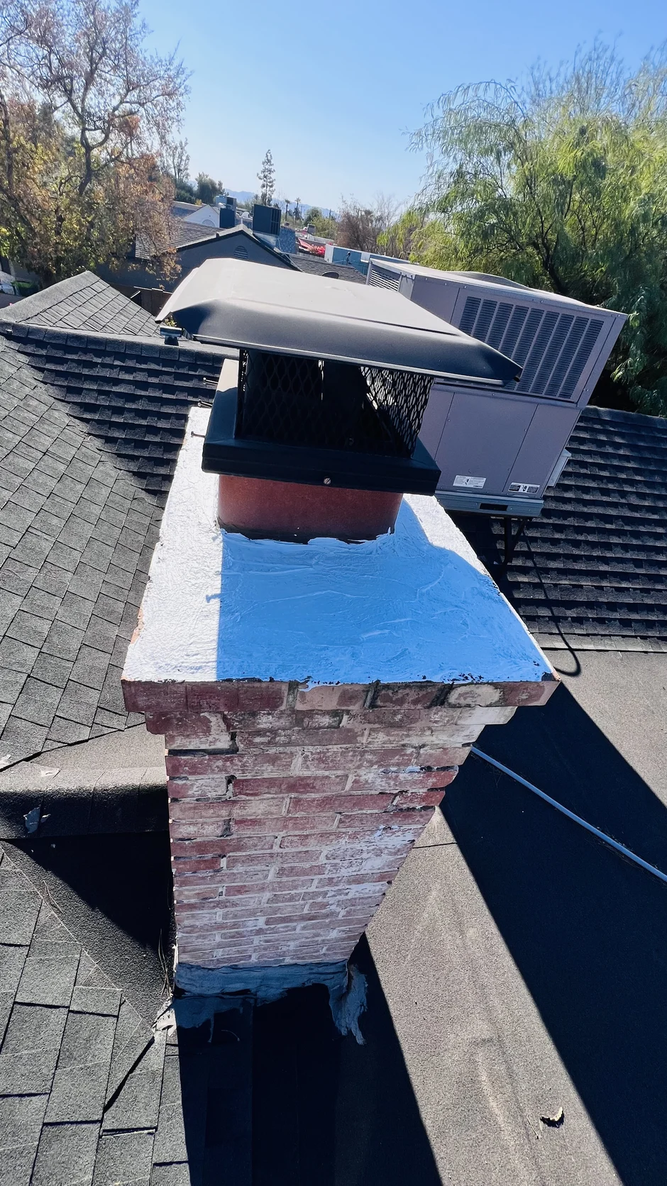 Metal cap on a brick chimney above a shingled roof