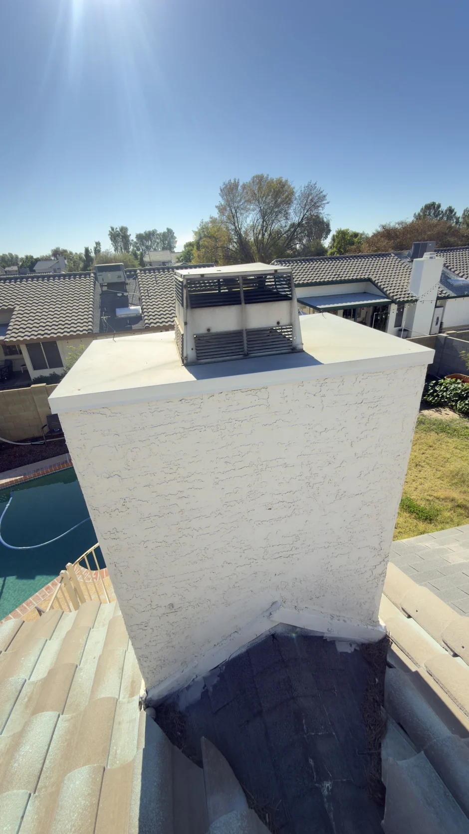 Capped chimney above a tile roof, with a swimming pool in the yard below