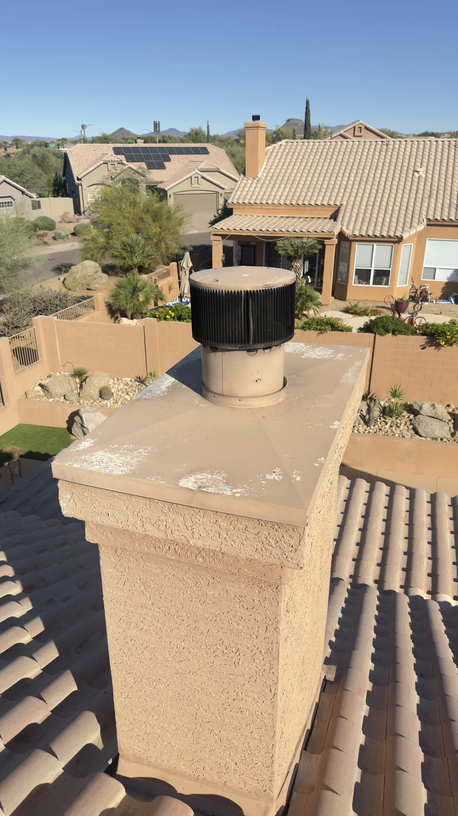 Capped chimney above tile roofs, with desert planting and mountains behind