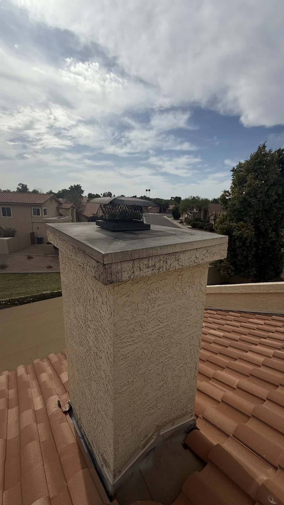 Capped chimney under overcast light above a barrel-tile roof