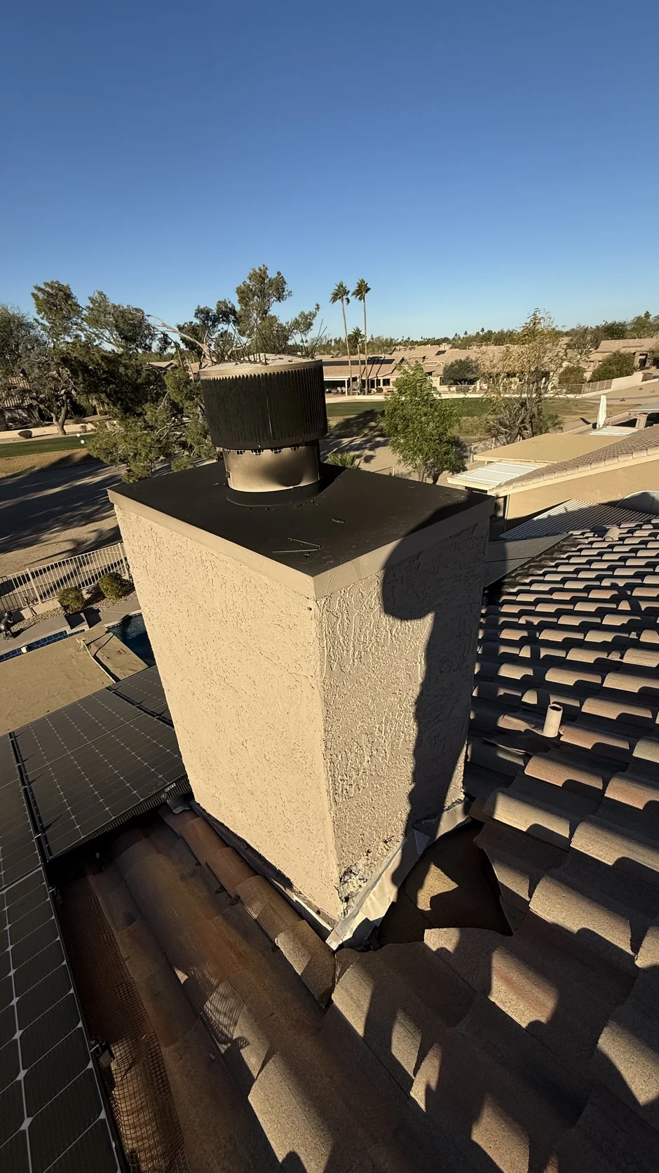 New chimney cap on a stucco chase, with palm trees and tile roofs behind