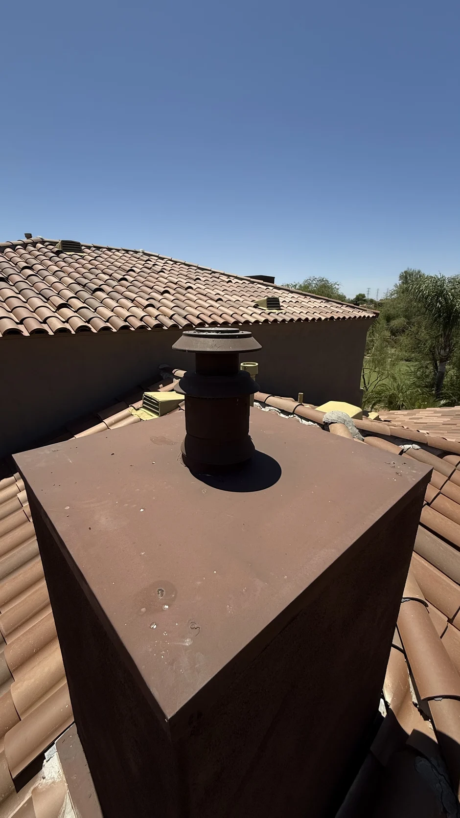 Metal chase shroud fitted over a chimney above a barrel-tile roof