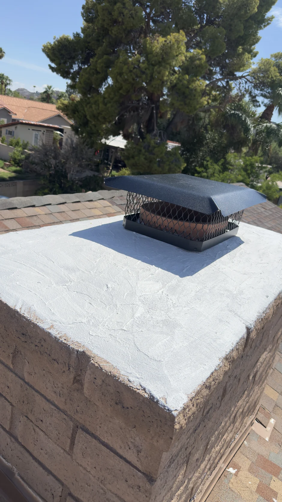 New white crown coating and cap on a brick chimney, tile roof at its base