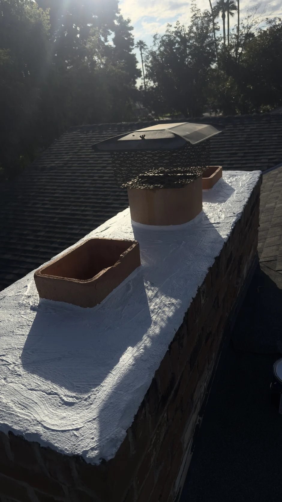 Freshly sealed white chimney crown with two clay flue tiles and a new cap