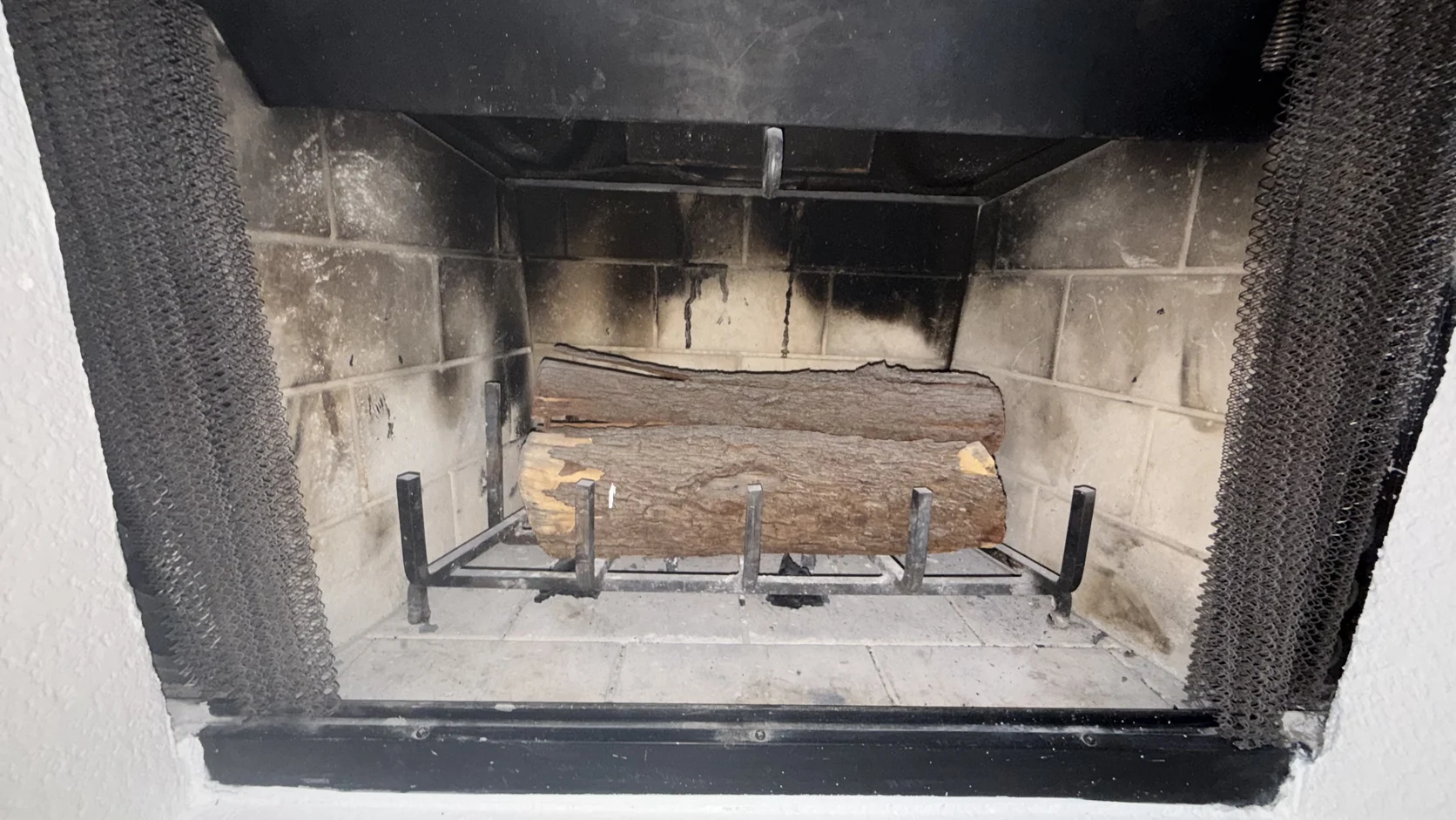 A single log on a grate in a soot-darkened firebox