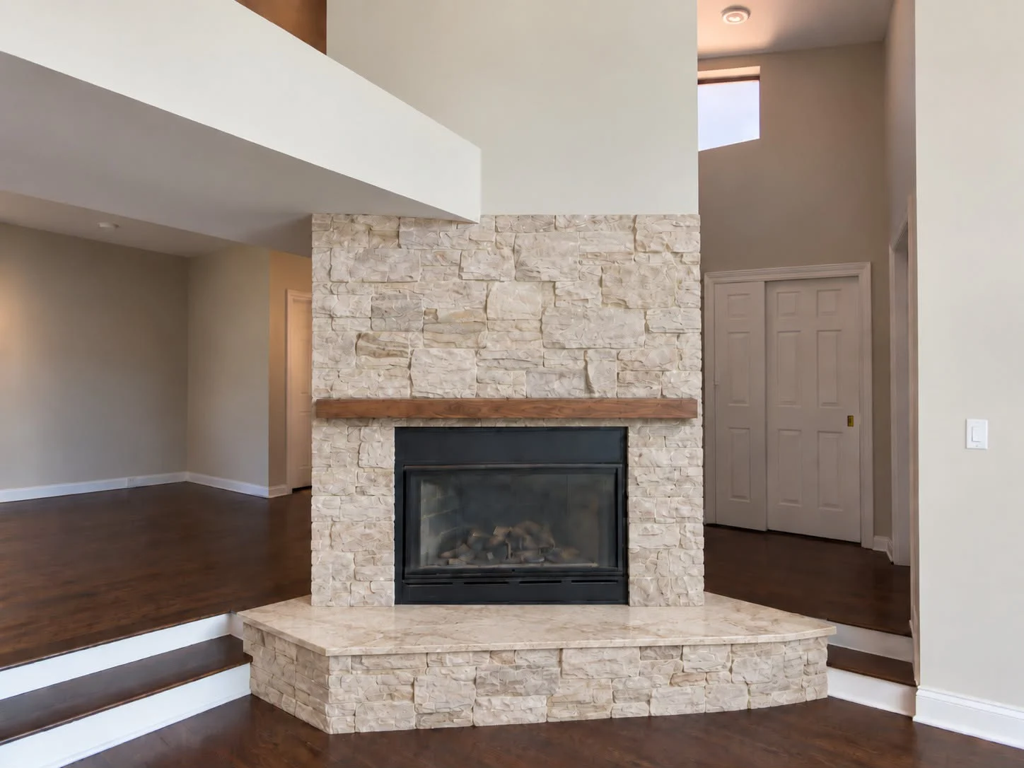 Stacked-stone corner fireplace seen from the side of an empty room
