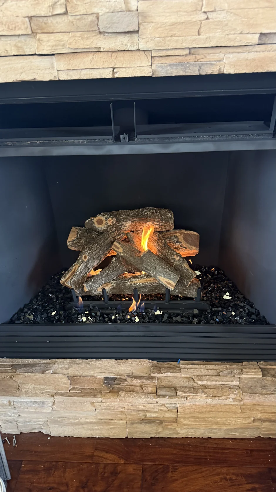 Gas log set in a fireplace with a stacked-stone surround