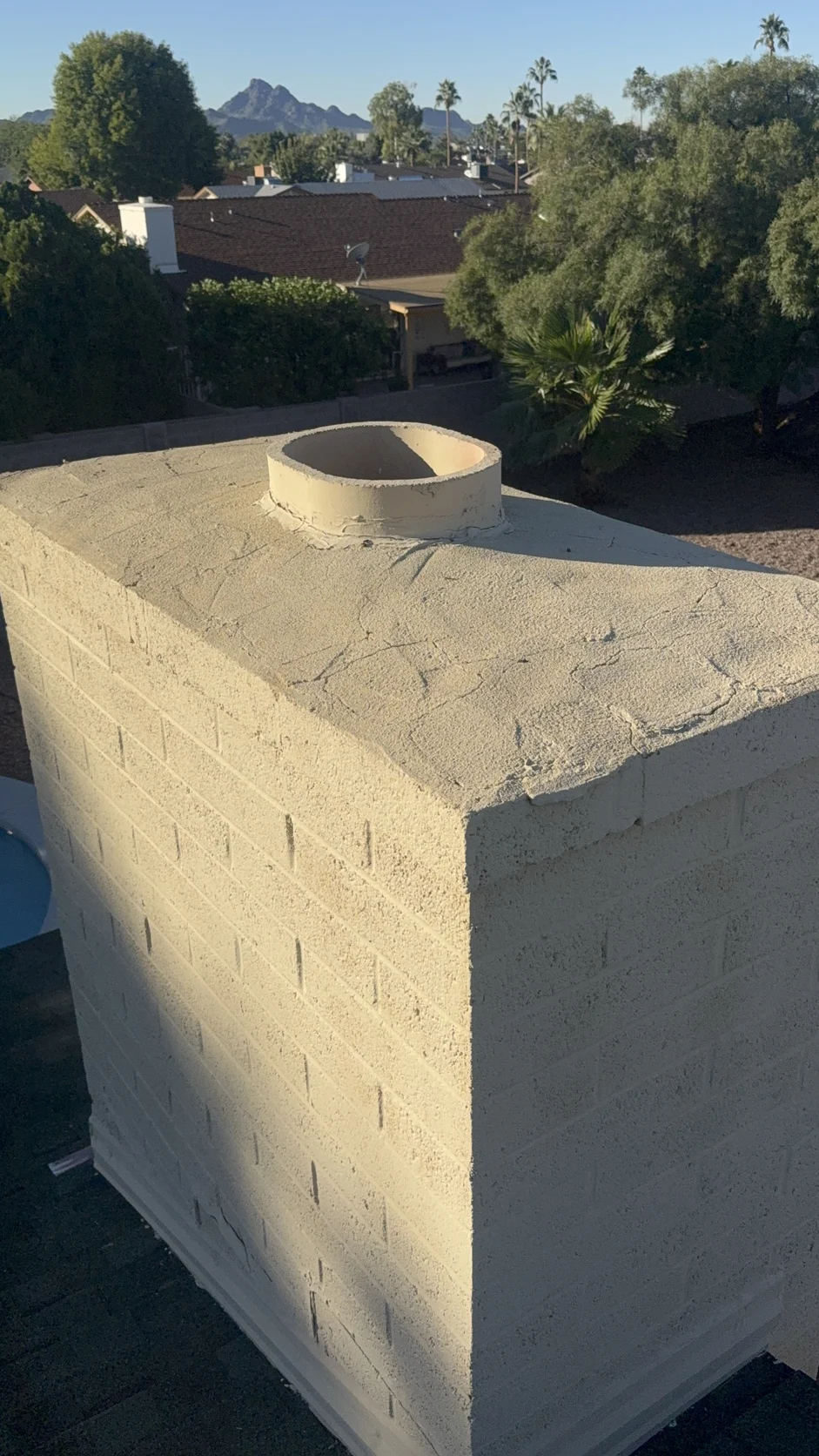 Stucco chimney with an open flue, palms and a mountain behind