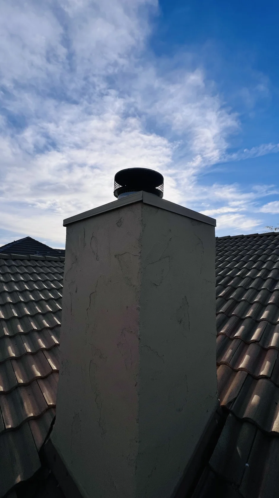 Round stainless cap on a stucco chimney above a barrel-tile roof