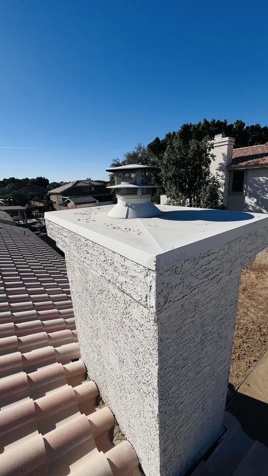 Fresh white crown coating and a new cap on a stucco chimney above a terracotta tile roof